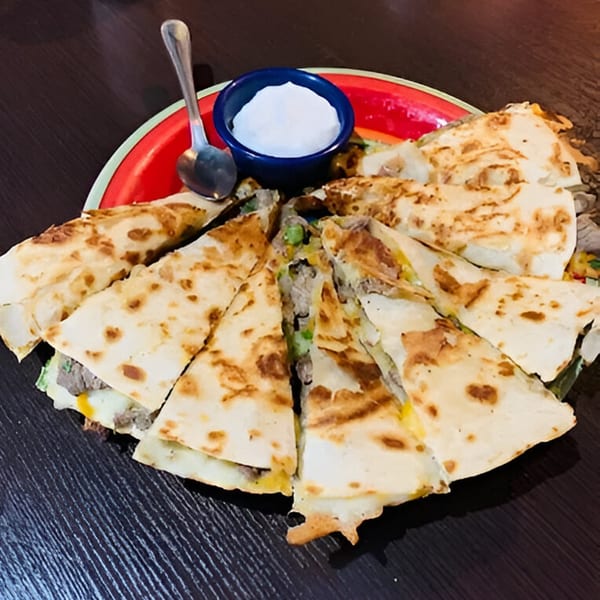 A platter of sliced quesadillas with meat and cheese, served with a side of sour cream.
