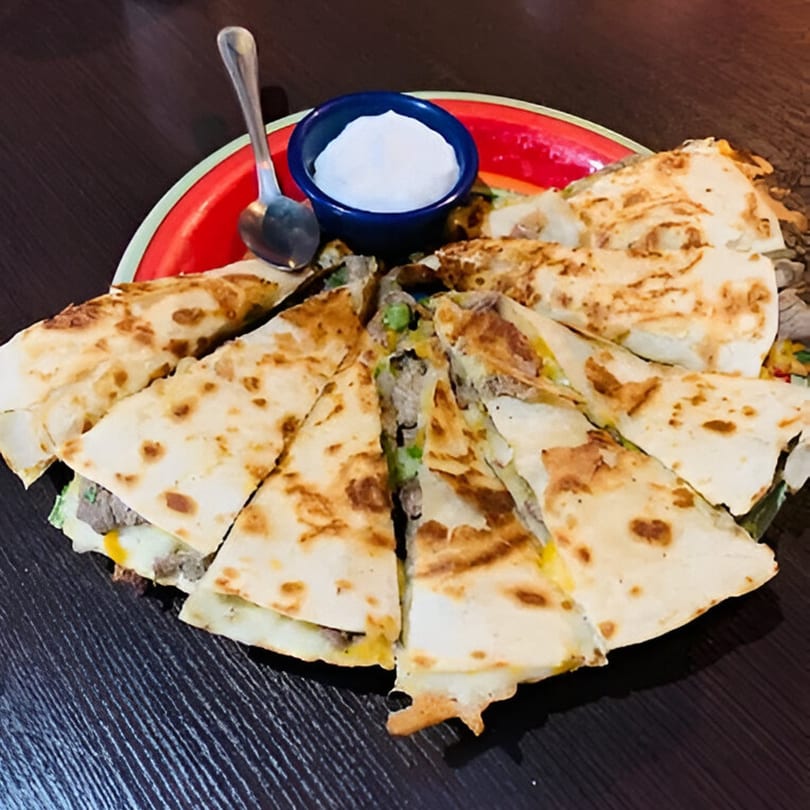 A platter of sliced quesadillas with meat and cheese, served with a side of sour cream.
