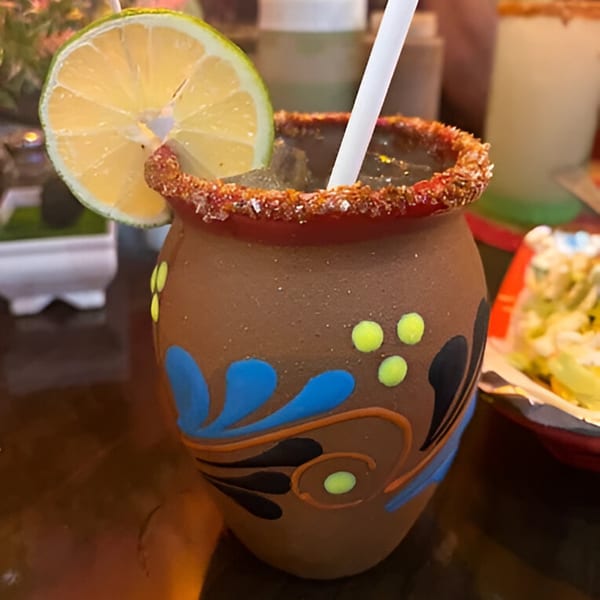 A Mexican cantarito cocktail in a decorated clay mug with a lime slice and chili-salt rim.