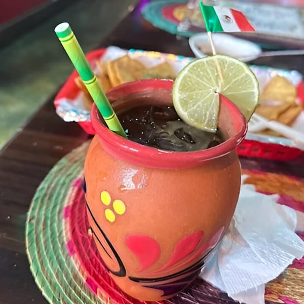 A traditional Mexican clay jar with a dark drink, lime slice, and a small Mexican flag.