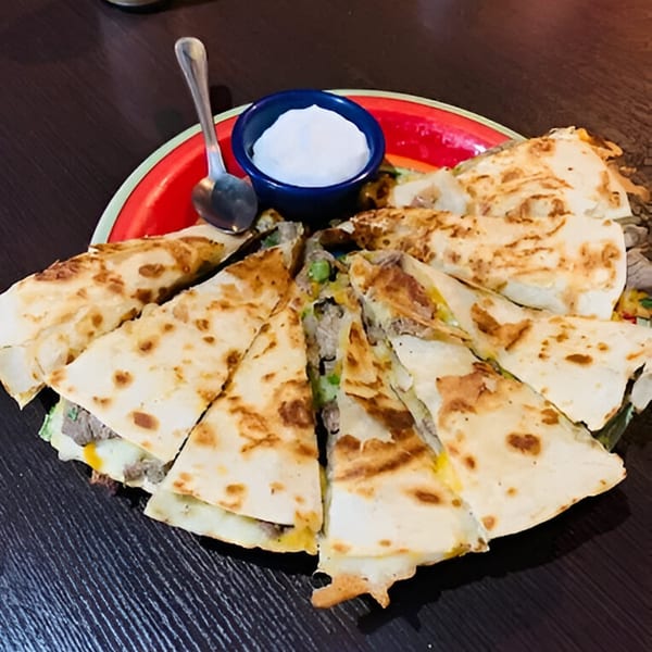 Taqueria los Jalapeňos' quesadilla, cut into wedges, with a side of sour cream on a red plate.