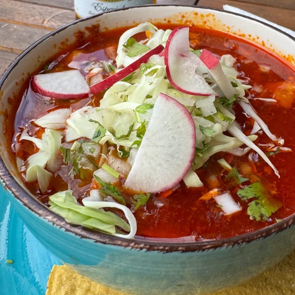 A close-up of a vibrant red Mexican pozole soup topped with shredded cabbage and radish slices.