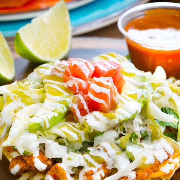 A Mexican tostada topped with shredded lettuce, diced tomatoes, and a drizzle of white sauce.