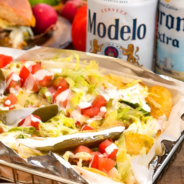 Taqueria los Jalapeňos' tacos with lettuce, tomatoes, sour cream, and pickles, with beer cans in the background.