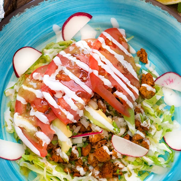 Mexican salad with chicken, lettuce, tomatoes, avocado, radishes, and crema on a blue plate.