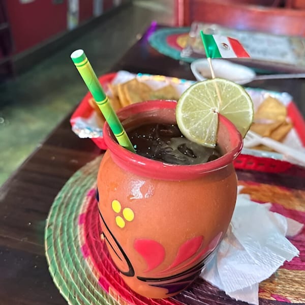 Mexican drink in a clay jar with a lime slice and a small Mexican flag, on a colorful placemat.
