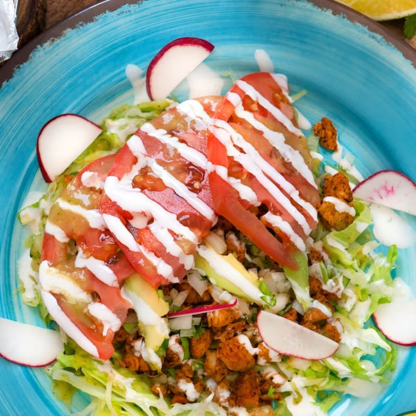 A vibrant Mexican salad with chicken, lettuce, tomatoes, avocado, radishes, and creamy dressing.