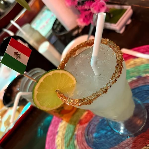 A margarita with a chili-lime rim, lime slice, and Mexican flag on a colorful placemat.