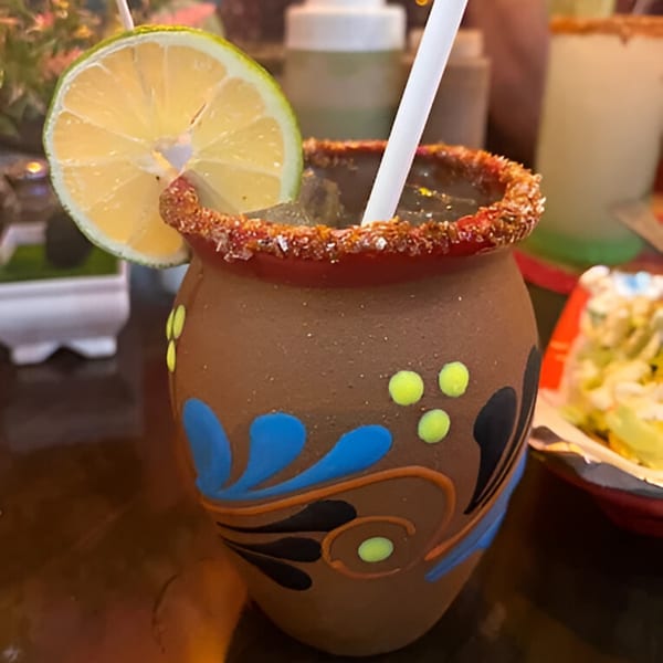 A Mexican cantarito cocktail in a decorated clay mug with a lime slice and chili-salt rim.