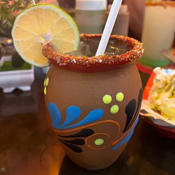 Mexican michelada in a decorated clay cup with a lime slice and chili salt rim.