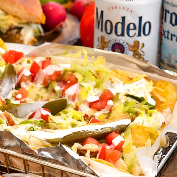 Mexican tacos with lettuce, tomatoes, sour cream, and jalapeños, with Modelo beer in the background.