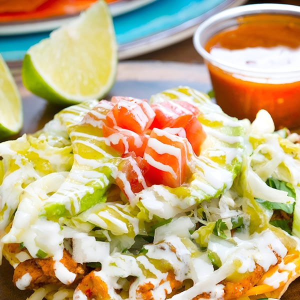 Close-up of a Mexican dish topped with lettuce, diced tomatoes, and white sauce, with lime wedges and salsa.