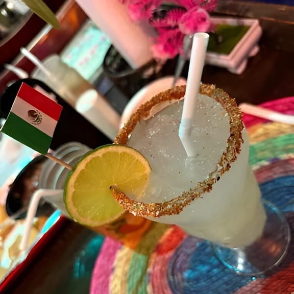 A frozen margarita with a lime slice and a Mexican flag on a colorful woven mat.