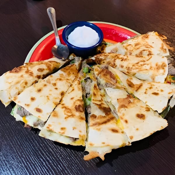 A red plate of sliced quesadillas with meat and vegetables, served with a side of sour cream.