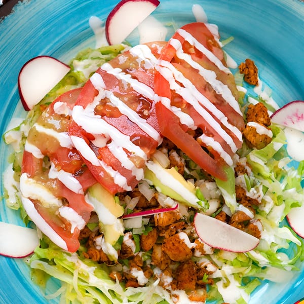 Mexican salad with chicken, lettuce, tomatoes, avocado, radishes, and crema on a blue plate.